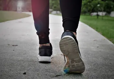fitness woman walking in public park, closeup on shoe with sunlight