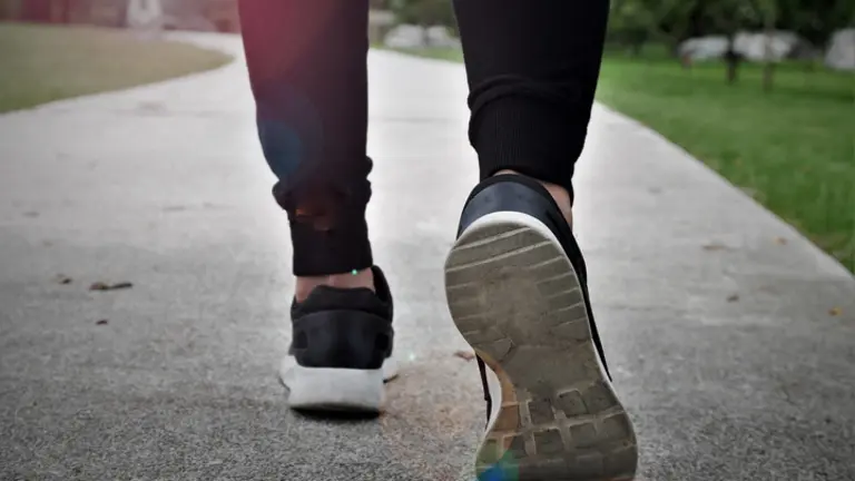 fitness woman walking in public park, closeup on shoe with sunlight